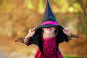 A portrait of a little girl in a witch costume hiding behind a black cap and showing her tongue. Halloween holiday. photo