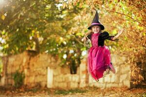 A little girl in a witch costume is jumping on the street. Halloween holiday. photo