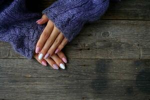 mujer es manos con un hermosa manicura, en un de punto suéter en un de madera antecedentes en. otoño tendencia, polaco beige y blanco polca puntos en uñas con gel polaco, goma laca. foto