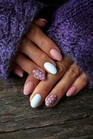 Women is hands with a beautiful manicure, in a violet knitted sweater on a wooden background in. Autumn trend, polish beige and white polka dots on nails with gel polish, shellac. photo