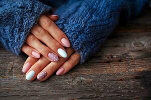 Women is hands with a beautiful manicure, in a knitted sweater on a wooden background in. Autumn trend, polish beige and white polka dots on nails with gel polish, shellac. photo