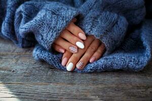 Women is hands with a beautiful manicure, in a knitted sweater on a wooden background in. Autumn trend, polish beige and white polka dots on nails with gel polish, shellac. photo
