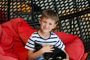 A little boy sits in a chair and holds a cat in his arms. photo