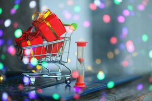 Hourglass and little goat with boxes of Christmas gifts on the background of a laptop. Online shopping. Boxing day concept.  Have time to buy. photo