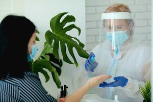 A manicurist in a protective mask and clothes in a beauty salon treats his hands with an antispecialist. Professional procedure. photo