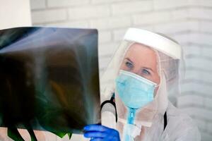 The doctor in PPE looks thoughtfully at the X-ray. photo