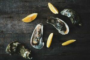 Close-up of fresh open raw oysters with lemon and ice on a wooden background. Healthy seafood. View from above. Copy space. photo