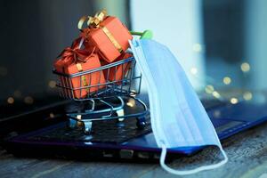 Small basket with boxes of Christmas gifts and a medical mask on photo