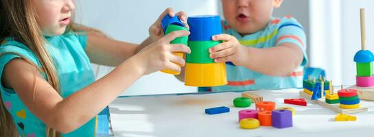 hermana ayuda pequeño hermano a montar el pirámide. educativo lógico juguetes para niños. montessori juegos para niño desarrollo. pequeño chico y niña jugar colores juguete. foto