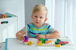 Little boy 2 years old is played with a wooden pyramid. Educational logic toys for children. Montessori games for child development. photo