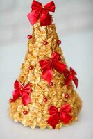 Children is craft. Christmas tree made of pasta, painted gold and decorated with a red bow. photo