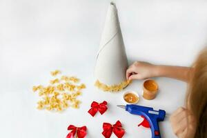 The child is hands glue pasta to the cone for making crafts. Christmas tree made from pasta.  Handmade, DIY. photo