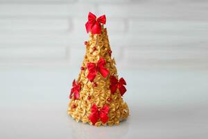 Children is craft. Christmas tree made of pasta, painted gold and decorated with a red bow.  Handmade, DIY.  Copy space. photo