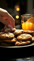 Close up Womans hand reaches for chocolate cookies, balancing them with orange juice Vertical Mobile Wallpaper AI Generated photo