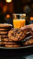 un cerca arriba de un mano agarrando chocolate galletas, mientras participación naranja jugo vertical móvil fondo de pantalla ai generado foto