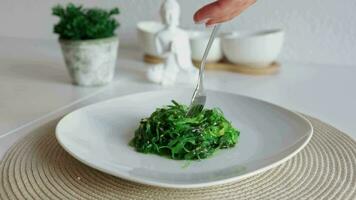 japonês wakame algas marinhas salada com sésamo em branco placa. mulher comendo saboroso algas marinhas salada com garfo video