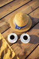 A hat and two cups of coffee stand on a pier near a sandy beach photo