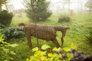 the figure of a goat from a straw stands in the middle of a green garden photo