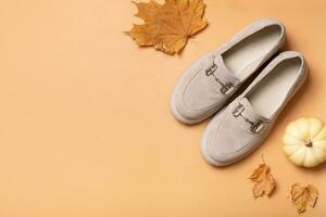 Casual fashion flat lay. Suede shoes with autumn leaves and pumpkin on orange background top view with copy space photo