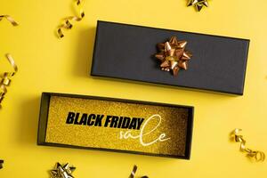 Black friday sale text in black gift box and festive decorations on yellow background flat lay, top view. photo