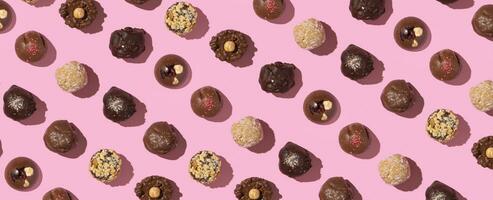 Chocolate craft candies pattern with nuts and dried fruits on pink background flat lay, top view photo