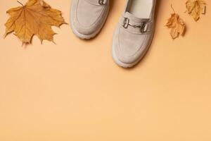 Suede woman's shoes with autumn leaves on orange background with copy space top view, flat lay. photo