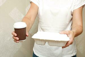 hembra manos participación un caja de almuerzo y un vaso de café foto