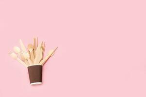 disposable bamboo cutlery in a paper cup on a pink background with copy space photo