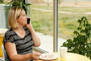 mujer en un café come postre y negociaciones en el teléfono a el mismo tiempo, teniendo un bocadillo en el correr foto