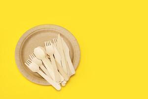 wooden disposable cutlery on a disposable paper plate on a yellow background with copy space photo