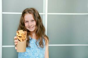 happy little girl holding out a paper cup with homemade curly cookies, school meals photo