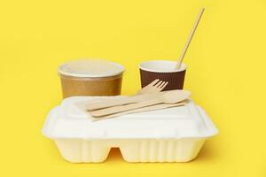 recycled disposable tableware set, soup container, glass with a straw, lunchbox, knife, fork, spoon on a yellow background photo