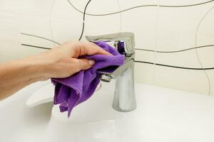 a woman's hand washes a faucet with a rag in the bathroom photo