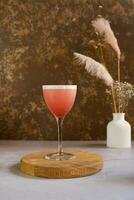 Alcoholic pink cocktail with foam on a wooden podium. Drinking still life. photo