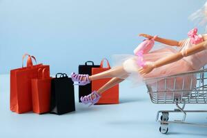 Doll in supermarket basket with shopping bag. Sale concept photo