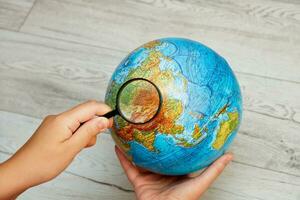 a woman's hand examines the globe through a magnifying glass photo