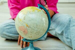 woman sitting on the floor looking at the globe through a magnifying glass photo