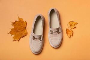 Suede woman's shoes with autumn leaves on orange background flat lay, top view. photo