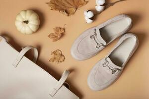 Suede shoes and bag with autumn leaves and pumpkin on orange background top view, flat lay photo