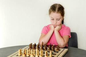 cute little girl sits thoughtfully at the table over chess photo
