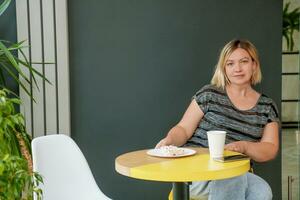 mujer en un café bebidas café en un papel taza y come pastel foto