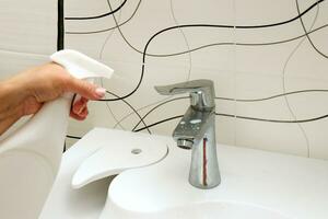 female hand spraying cleaning agent on sink and faucet in bathroom photo