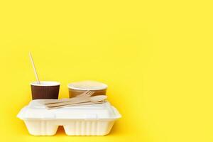 recycled disposable tableware set, soup container, glass with a straw, lunchbox, knife, fork, spoon on a yellow background photo