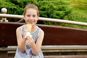 pequeño linda niña comiendo hielo crema en el parque en un banco foto