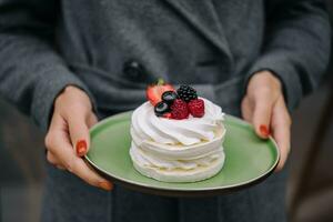 Pavlova meringue cake with fresh berries on a plate in female hands photo