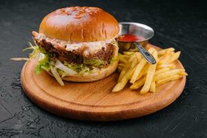 Delicious hamburger with cheese sauce and french fries on wooden table photo