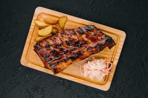 Pork loin ribs served on chopping board and potato wedges photo