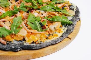 Black pizza with seafood on a wooden round plate on a white photo
