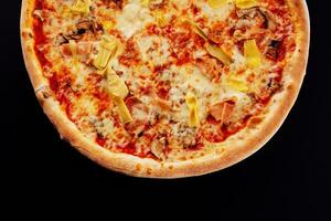 italian pizza with sliced ham and artichokes on black background photo