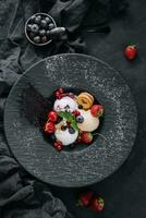 Vanilla ice cream scoops with fresh berries on black plate photo